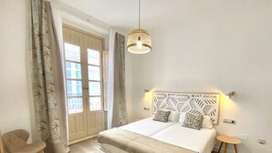Un dormitorio con cama, una silla, una mesita y una lámpara colgante.