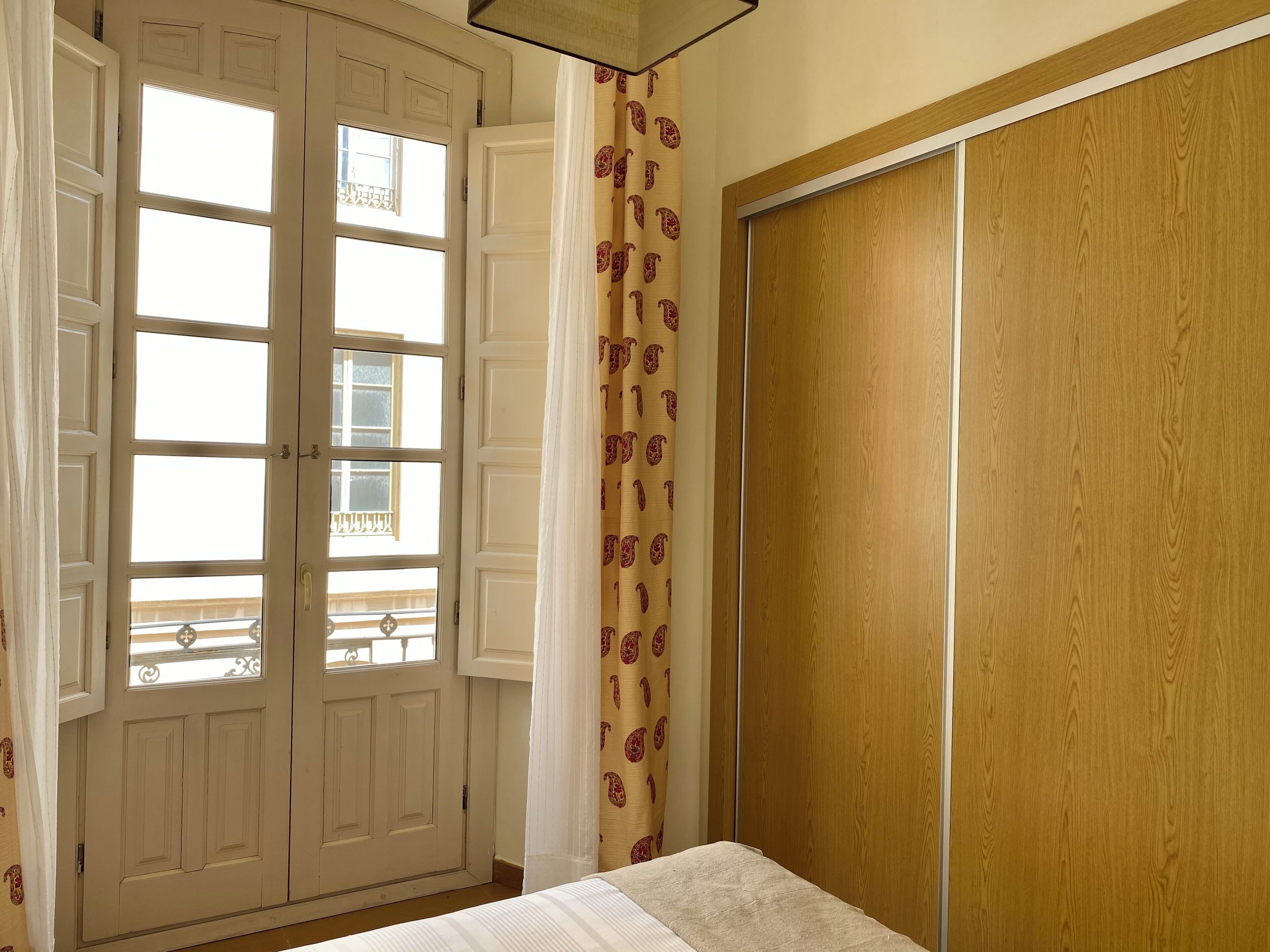 Una habitación con cama, armario y ventana con vistas a un balcón.