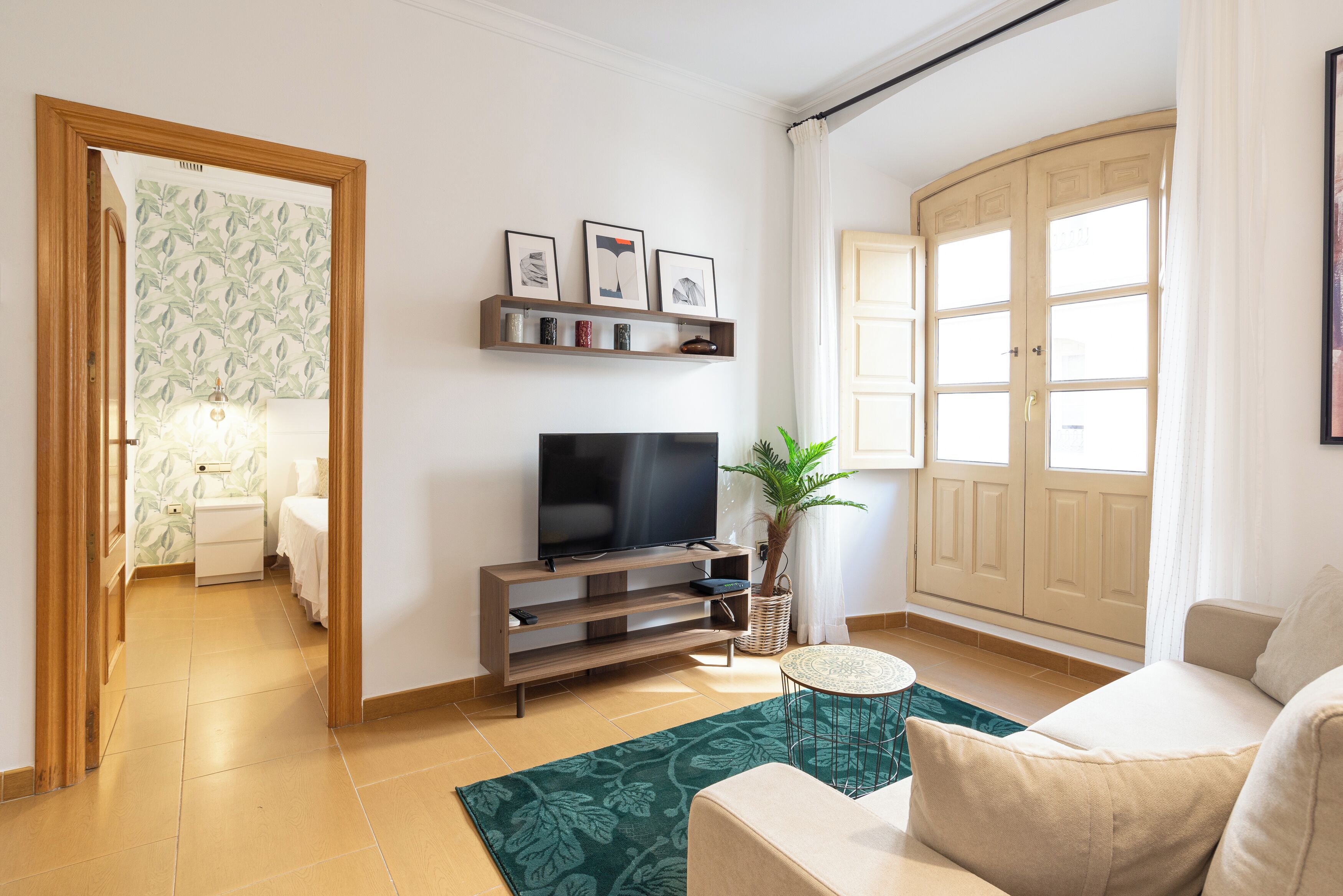Ein Wohnzimmer mit Fernseher, Sofa und einem Teppich mit grünem Muster.