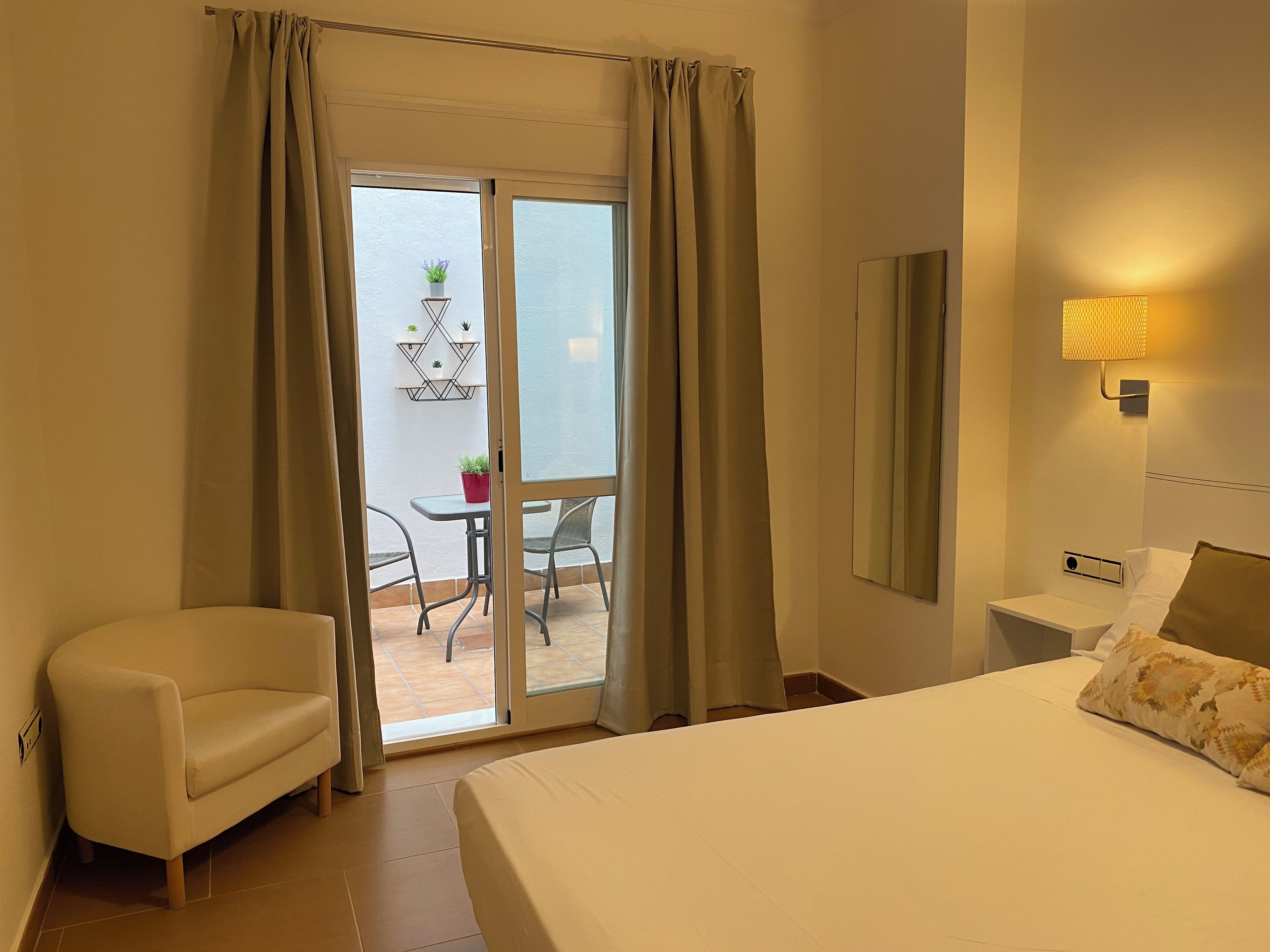 A hotel room with a bed, a chair, a small table with plants, and a balcony with a table and chairs.