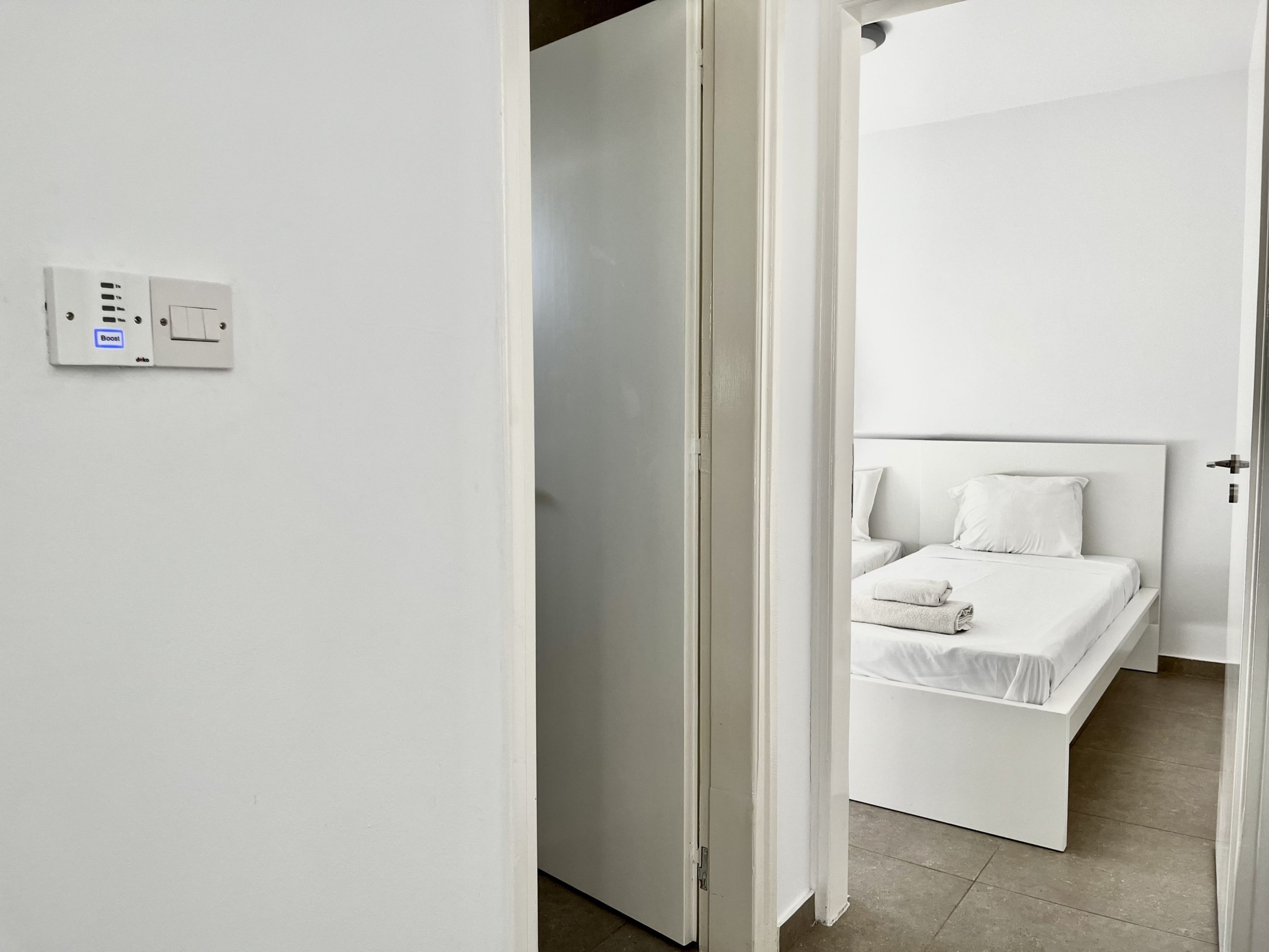 A modern, minimalistic hotel room with a large bed, a bedside table, and a white door.