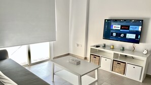 A modern living room with a white sofa, a coffee table, and a flat-screen TV mounted on the wall. - 04 AN - Stay Ease Apartment (Ayia Napa)