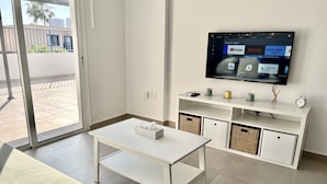 A modern living room with a white sofa, a white coffee table, and a TV mounted on the wall displaying popular apps. - 04 AN - Stay Ease Apartment (Ayia Napa)