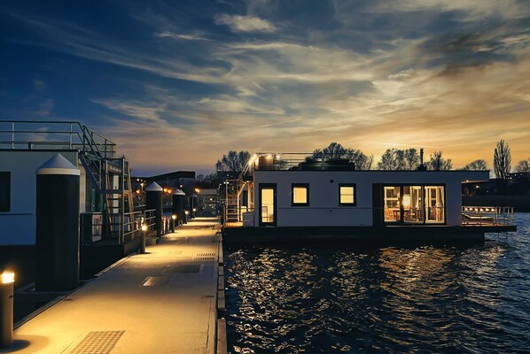 A waterfront building with a dock extending into the water, featuring multiple levels and a glass facade. - Hausboot am Saaler Bodden, Ribnitz-damgarten (Ribnitz-Damgarten)