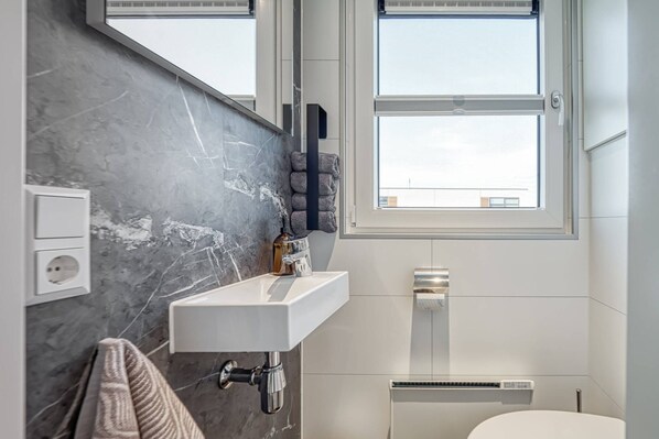 Une salle de bain moderne avec un mur en marbre, un lavabo blanc, une serviette et une fenêtre donnant sur le ciel.