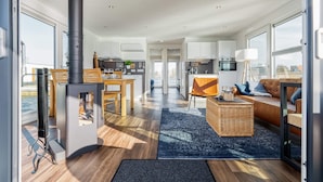 A modern living room with a fireplace, a dining area, and a kitchen visible through an open door.