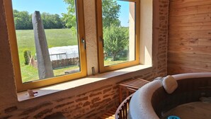 A hot tub in a rustic room with a window overlooking a garden.