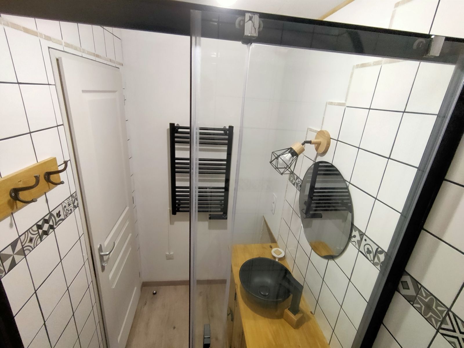 A bathroom with a glass shower door, a wooden vanity with a black sink, and a towel rack.