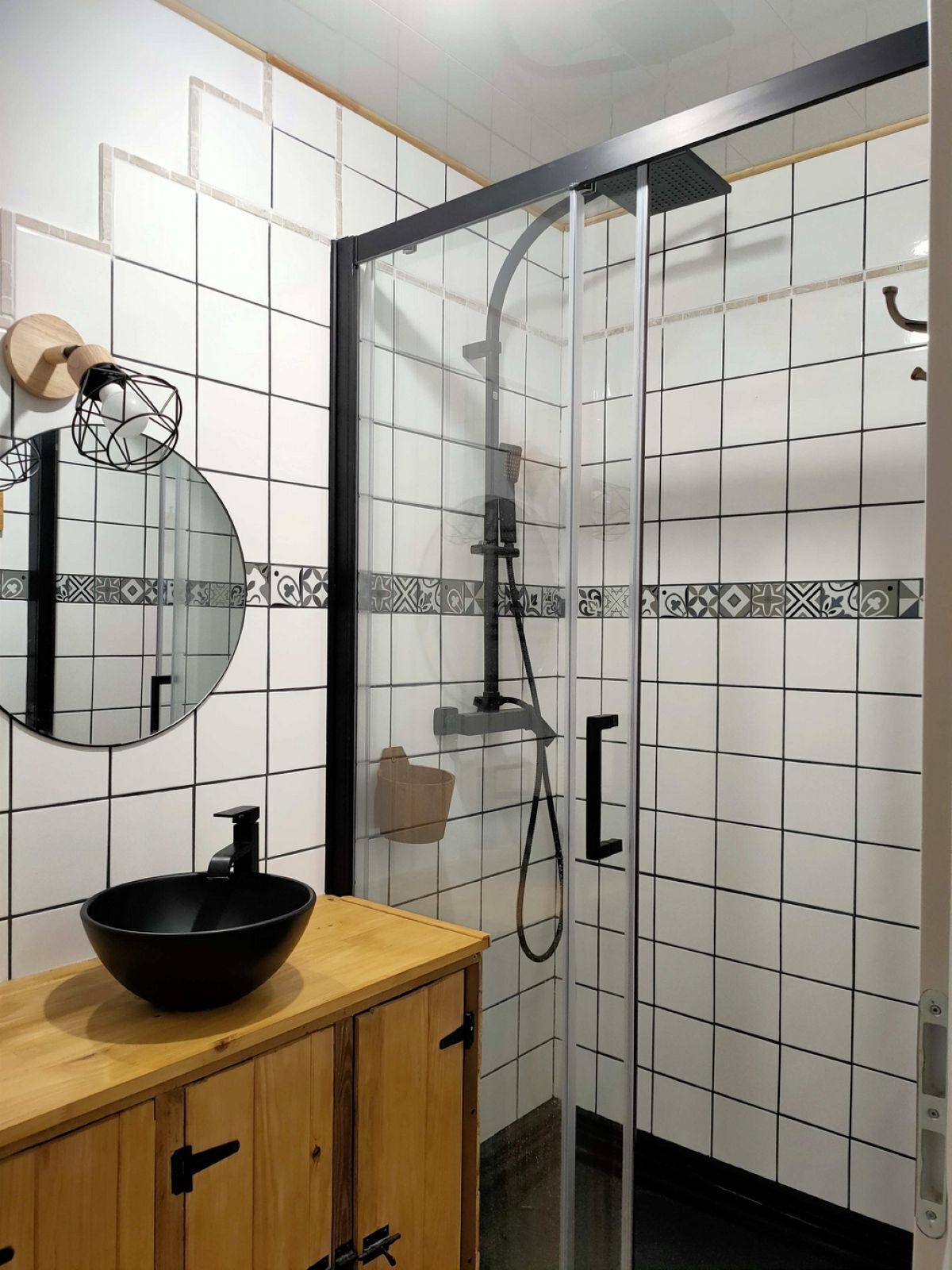 Une salle de bain avec un lavabo noir, un miroir rond et une douche dotée d’une porte en verre.