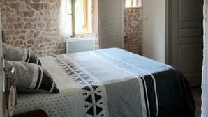 A bedroom with a stone wall, a bed with patterned bedding, a wooden headboard, a hanging light fixture, and a door leading to another room.