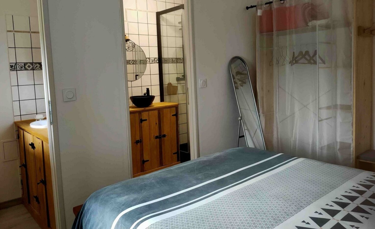 A bedroom with a bed, a wooden cabinet, a mirror, and a shower area.