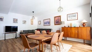 Una sala de estar moderna con comedor, que incluye una mesa de madera, sillas de cuero, un sofá gris y un televisor sobre un mueble.