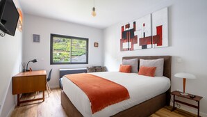 Un dormitorio con una cama grande, un escritorio, una silla, un televisor y una ventana con vistas a zonas verdes.