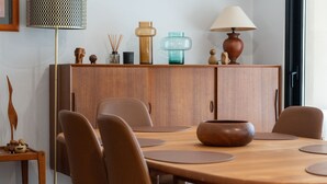 Un comedor con una mesa de madera, sillas marrones y un armario con adornos.