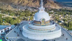 Eine große, weiße, mehrstufige Stupa mit aufwendigen Verzierungen, umgeben von einem gepflasterten Bereich mit Passanten.
