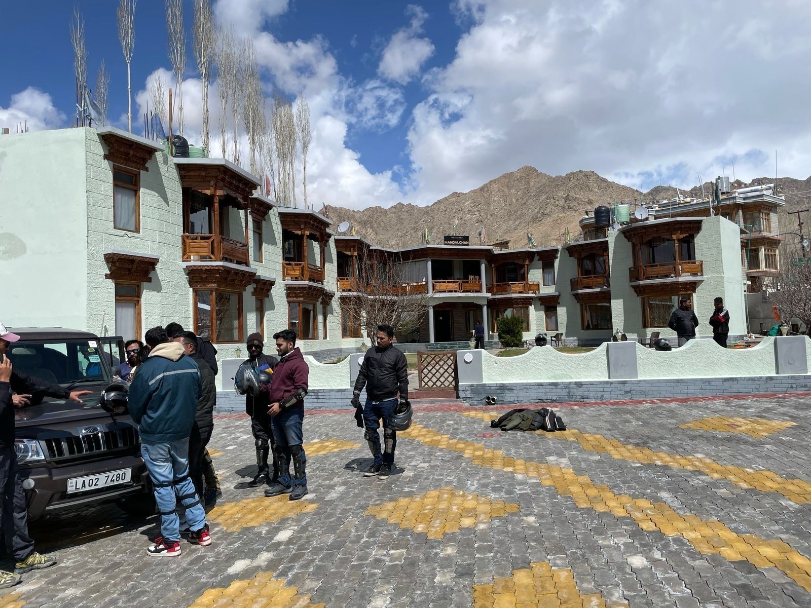 A hotel with multiple balconies, a paved courtyard, and mountainous background.