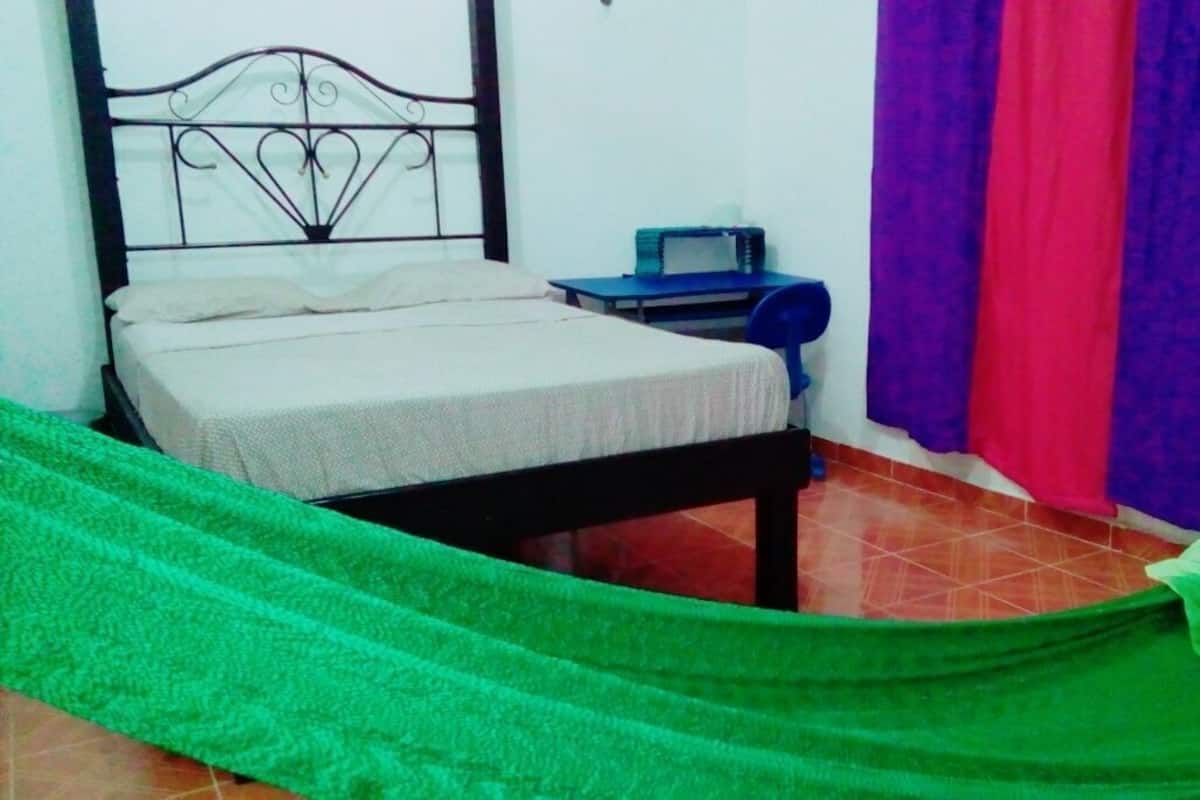 A room with a bed, a small desk with a chair, and a window with curtains.