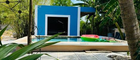 Un espace piscine doté d’une structure bleue, entouré d’une végétation tropicale.