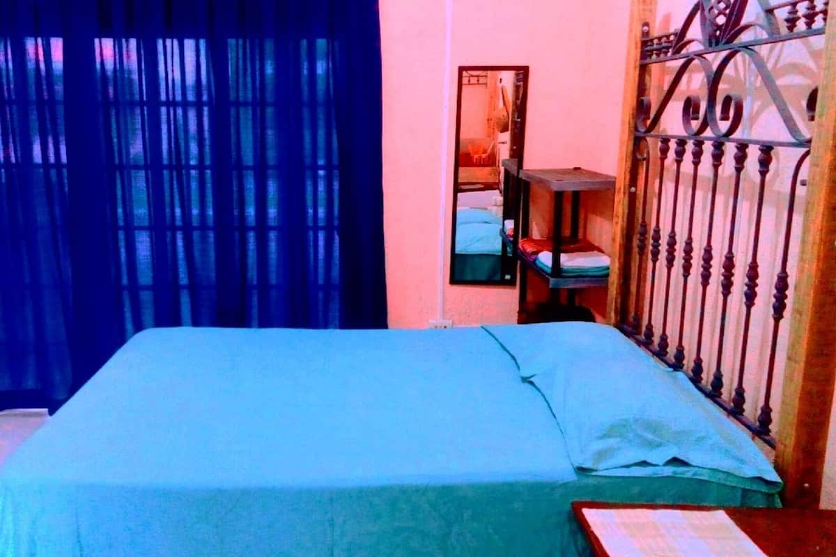 A room with a bed, a window with curtains, a mirror, and a metal gate.