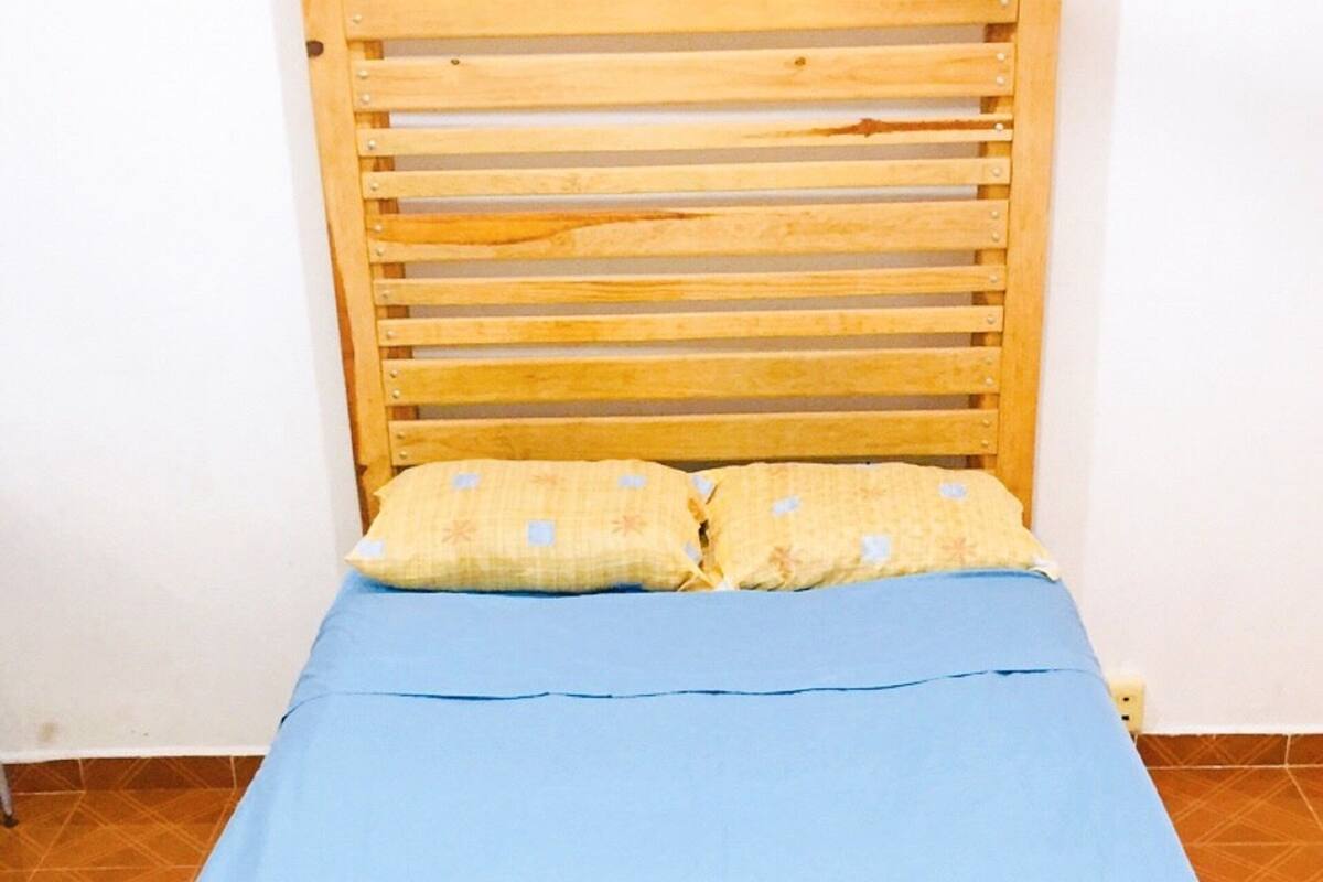 A wooden bed with a slatted headboard, a blue mattress, and two pillows.