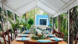 Un espacio de comedor techado con una mesa larga dispuesta para seis personas, rodeada de sillas de madera con asientos acolchados.