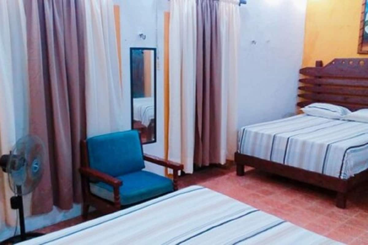 A bedroom with a bed, a chair, a fan, and curtains.