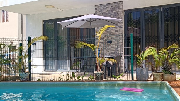 A swimming pool with a pink float, surrounded by potted plants and a metal fence. - Charming 2-bedroom villa with WiFi and AC in Grand Baie (Grand Baie)