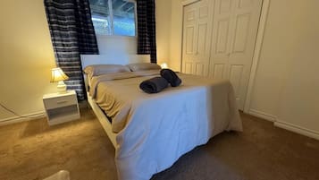 Un lit bien fait, avec une tête de lit blanche, une table de chevet avec une lampe et une fenêtre avec des rideaux.