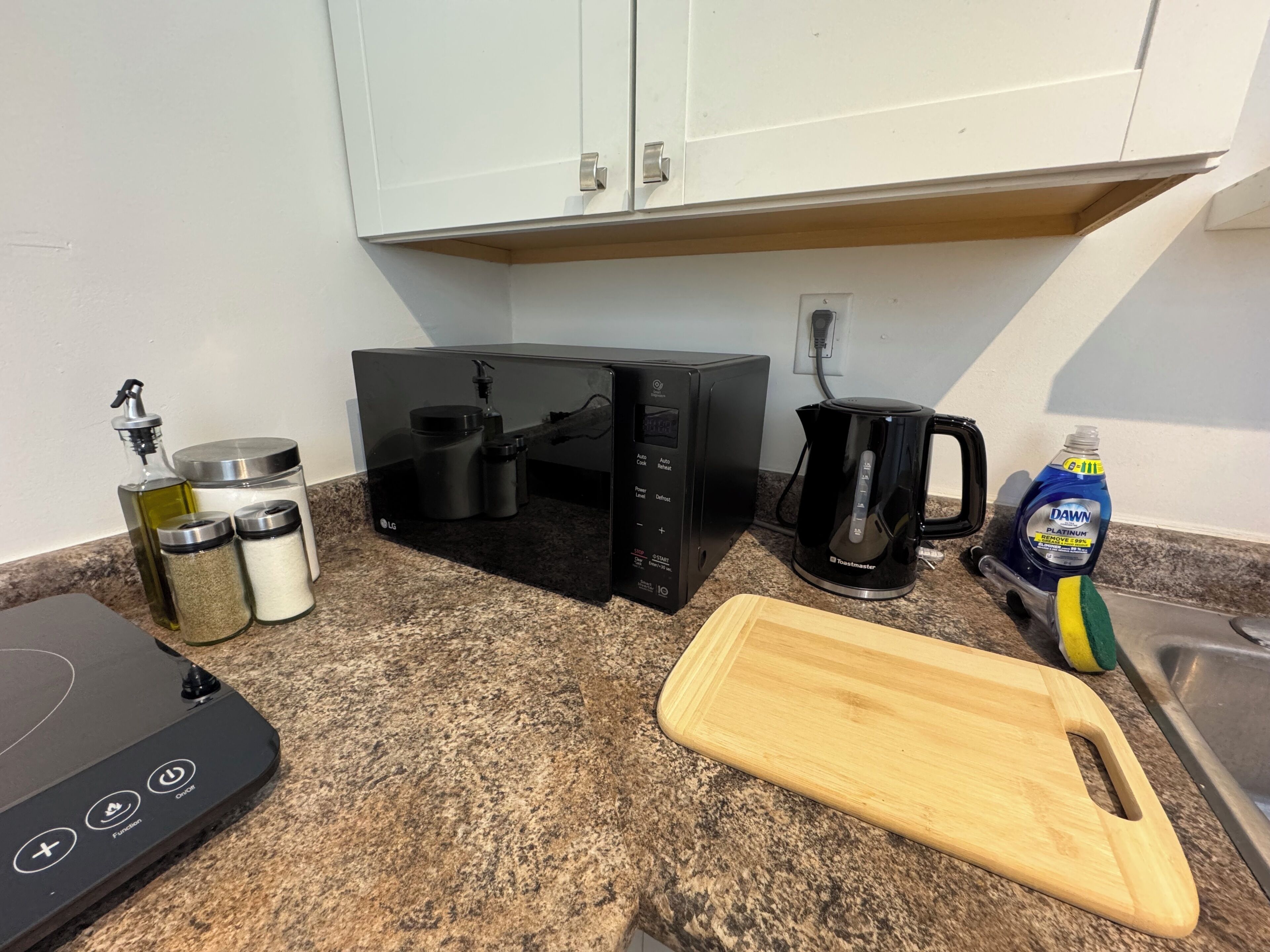 Una cocina equipada con microondas, tostadora, cafetera y tabla de cortar.