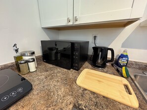 Una cocina equipada con microondas, tostadora, cafetera y tabla de cortar.