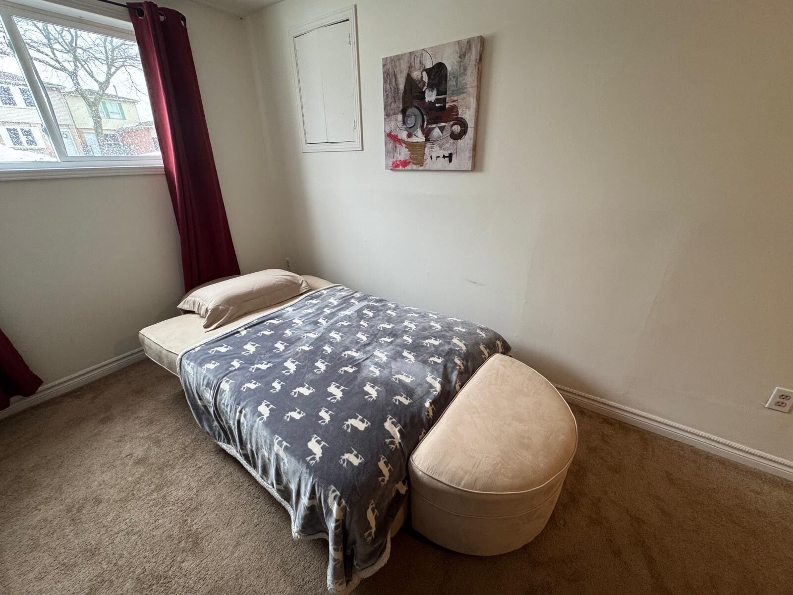 Une chambre à coucher avec un lit, une fenêtre avec des rideaux, une œuvre d’art accrochée au mur et un sol recouvert d’une moquette.