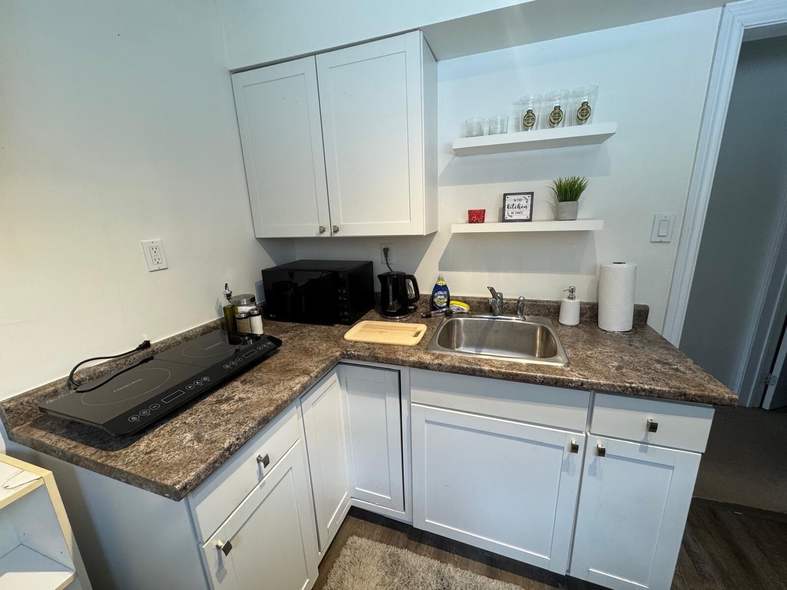 A kitchen with white cabinets, a granite countertop, a black microwave, a sink, and a coffee maker.