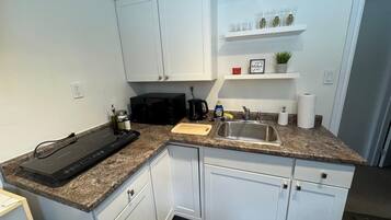 A kitchen with white cabinets, a granite countertop, a black microwave, a sink, and a coffee maker.