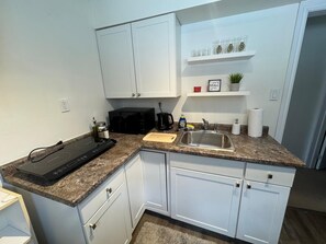Une cuisine avec des meubles blancs, un plan de travail en granit, un micro-ondes noir, un évier et une machine à café.