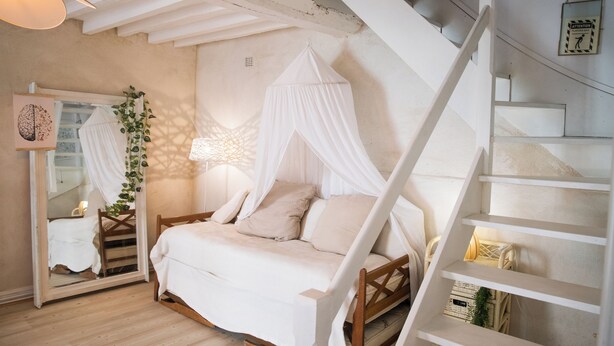 A bedroom with a canopy bed, a staircase, and a mirror.