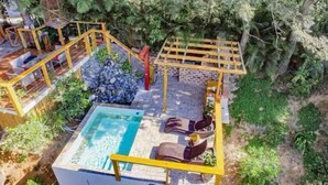 A pool area with a wooden pergola, a small seating area with chairs, and a stone wall.