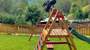 A wooden swing set in a grassy area with a view of mountains and trees.
