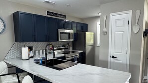 A modern kitchen with dark blue cabinets, a stainless steel refrigerator, a microwave, and a sink with a marble countertop. - BEAUTIFUL FULLY REMODELED WALK-IN 1 BEDROOM CONDO WITH FULL KITCHEN (Branson)