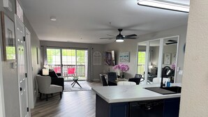A modern kitchen with a dishwasher, a dining area with chairs, and a view of the outdoors through large sliding doors. - BEAUTIFUL FULLY REMODELED WALK-IN 1 BEDROOM CONDO WITH FULL KITCHEN (Branson)