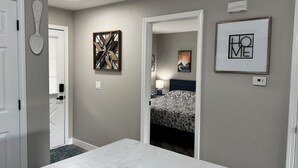 A hotel room with a bed, a desk, and a door leading to another room. There are wall art pieces and a light fixture on the ceiling. - BEAUTIFUL FULLY REMODELED WALK-IN 1 BEDROOM CONDO WITH FULL KITCHEN (Branson)