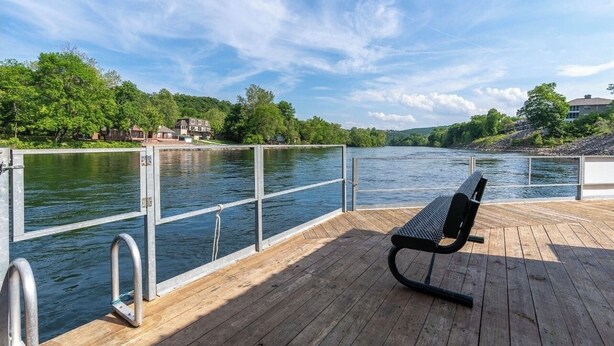 A wooden deck with a metal railing overlooking a river, a bench, and houses in the background. - BEAUTIFUL FULLY REMODELED WALK-IN 1 BEDROOM CONDO WITH FULL KITCHEN (Branson)