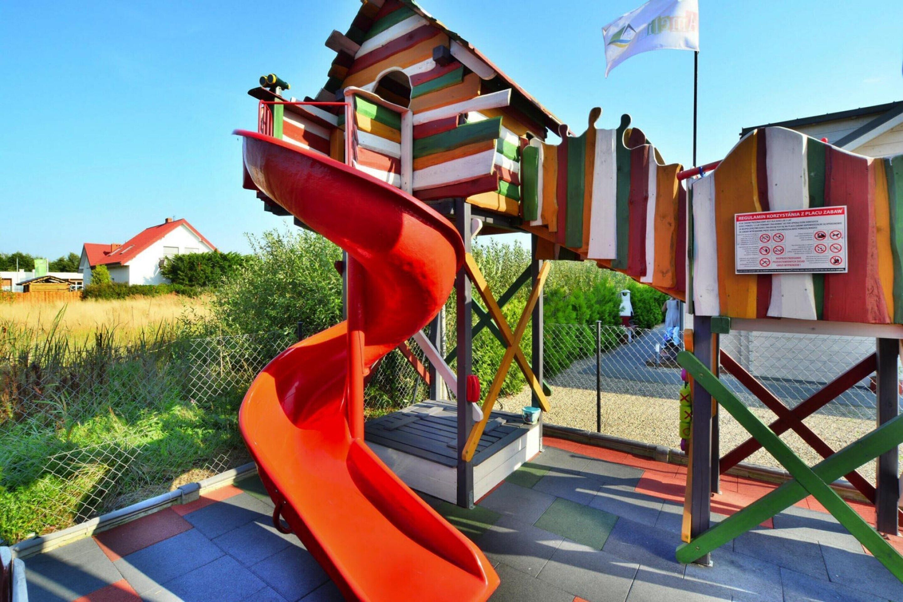 A playground with a red slide and a wooden climbing structure.