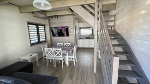 A compact living space with a dining area, a sofa, a TV, and a staircase.