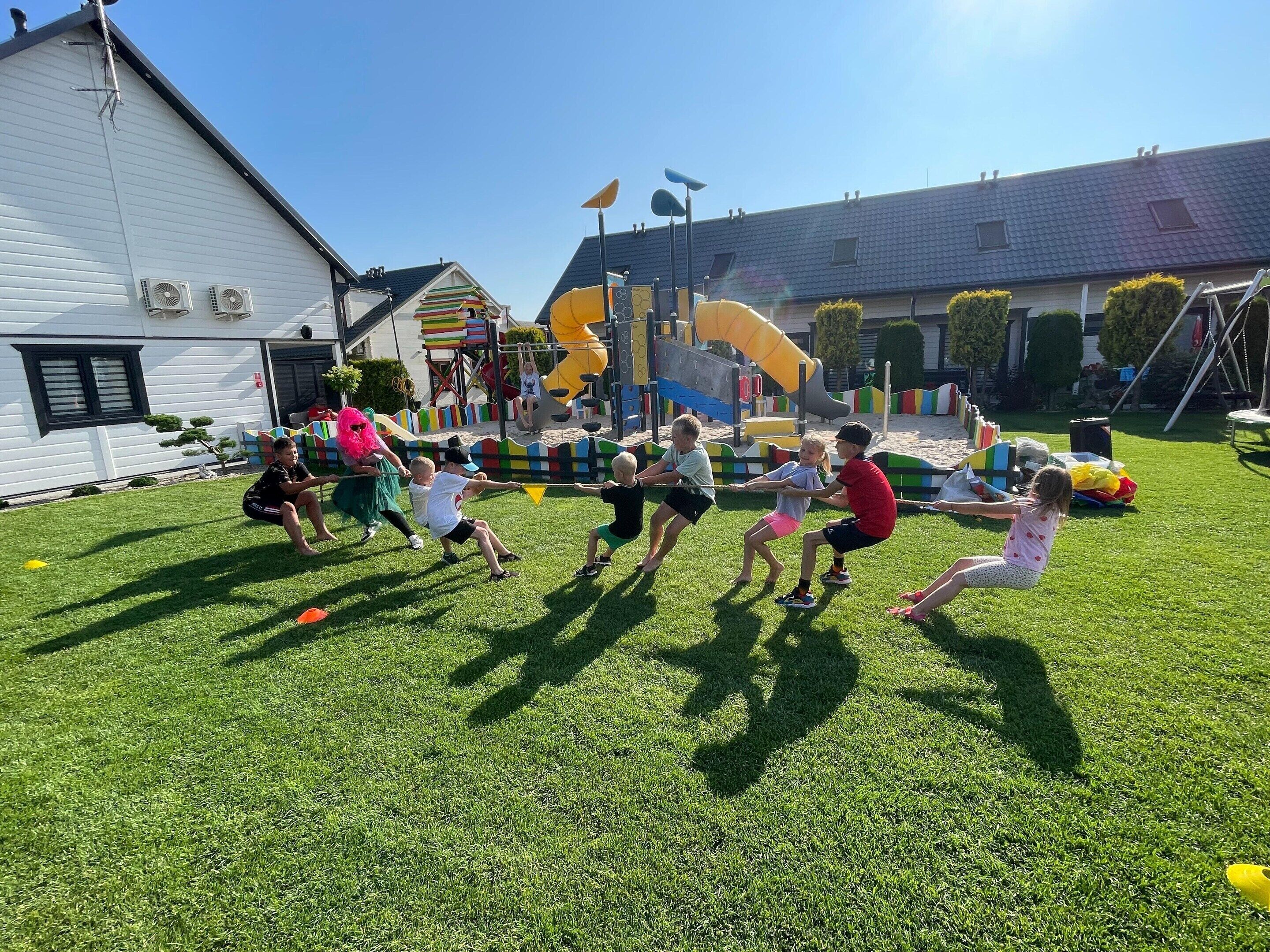 Children playing on a grassy field with playground equipment in the background.