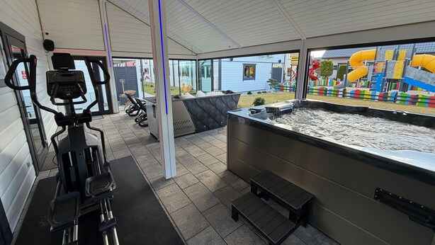 A gym with exercise equipment, a hot tub, and a view of a playground.