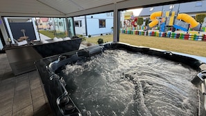 A hot tub with a view of a colorful playground and a house in the background.