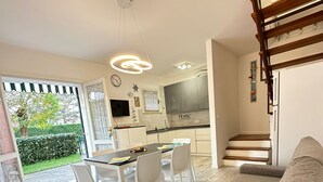 A modern kitchen with white cabinets, a dining area with a table and chairs, and a staircase leading to an upper level. - Modern two Level Villa With Playground and Pool (San Michele al Tagliamento)