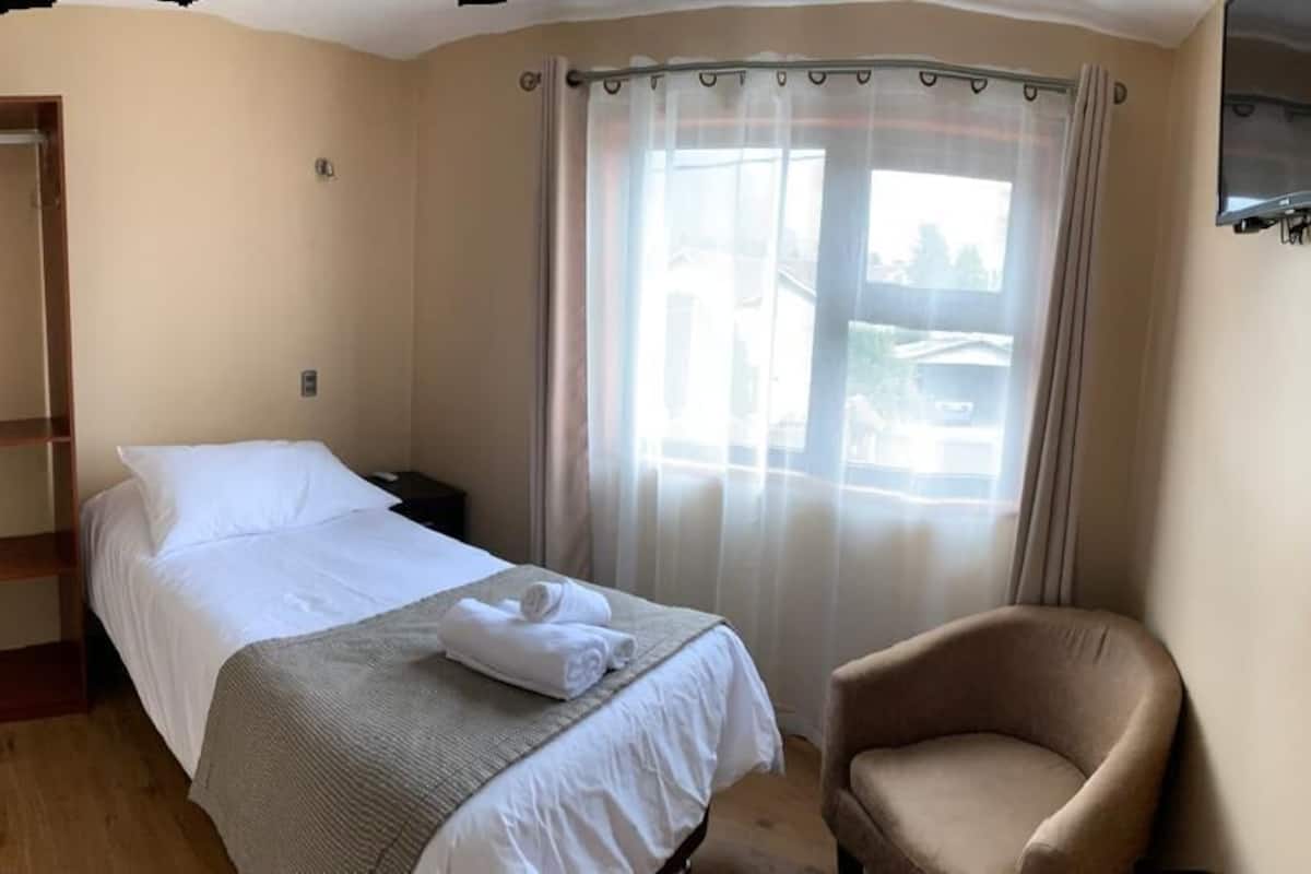 A hotel room with a bed, a chair, a TV, and a window with curtains.
