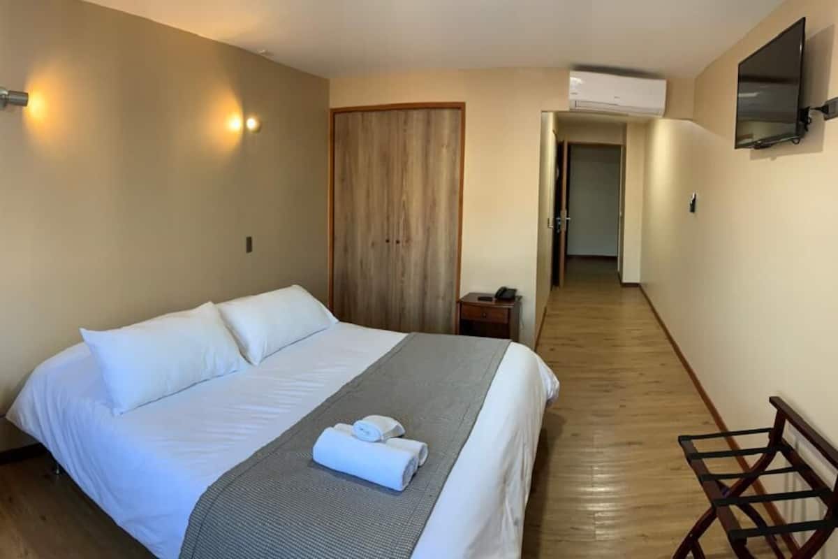 A hotel room with a bed, a bedside table, a TV mounted on the wall, and a wooden floor.