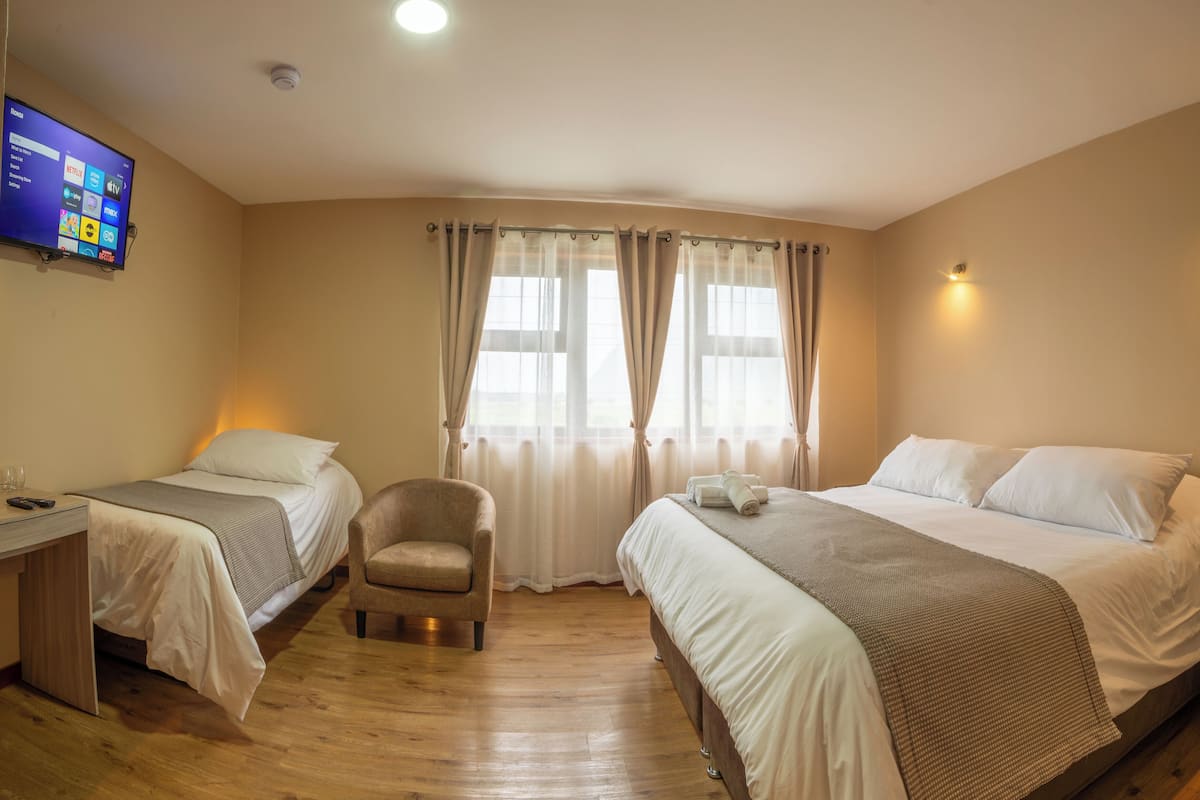 A hotel room with two beds, a chair, a desk, and a TV displaying a streaming service interface.